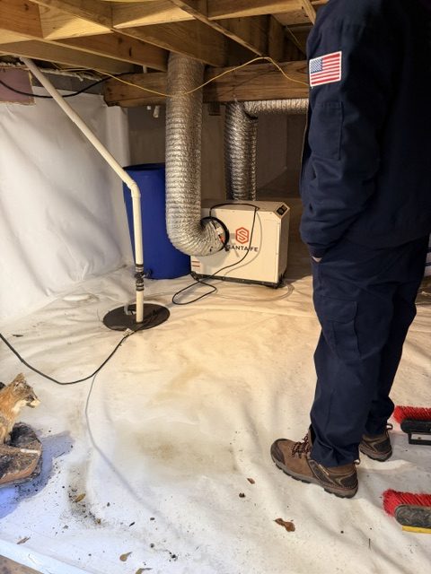 Crawl space drying with American flag uniformed technician next to dehumidifier and HVAC ducting