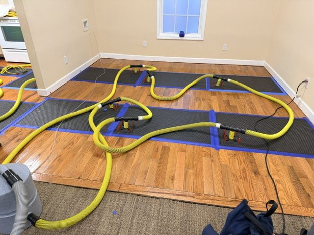 Active water spreading across kitchen hardwood floor showing water damage in progress before extraction